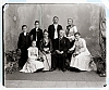 Ateliér. foto - 8 členů (pán sedící s medalilí na prsou, ženy - kytice, ústřední pár drží hole s ozdobnou hlavicí)
