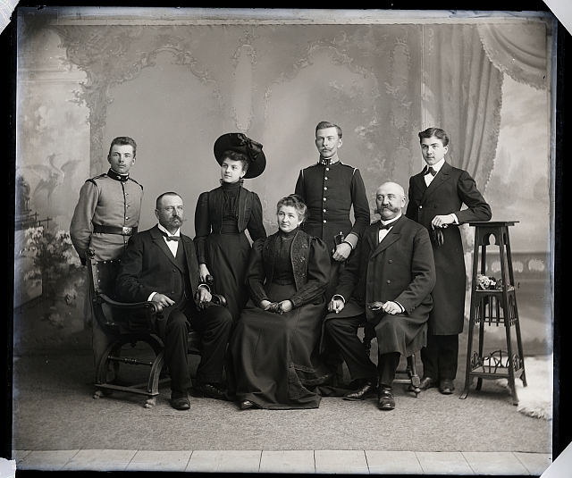 Ateliérový snímek - rodina - 5 mužů (2 uniforma), 1 stará dáma, 1 mladá dáma v klobouku  Na krabičce:  200 v kroužku, 598  - Skupina typografů  - tamburaši s p. Heřmánke... skupina