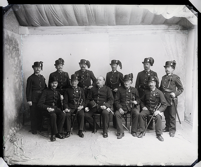 Ateliérový snímek - 11 mužů v uniformě, šavle  Na krabičce:  193 v kroužku, 609  Abiter neisnorem a far Vojta, továrník Kaž. 18... skupina