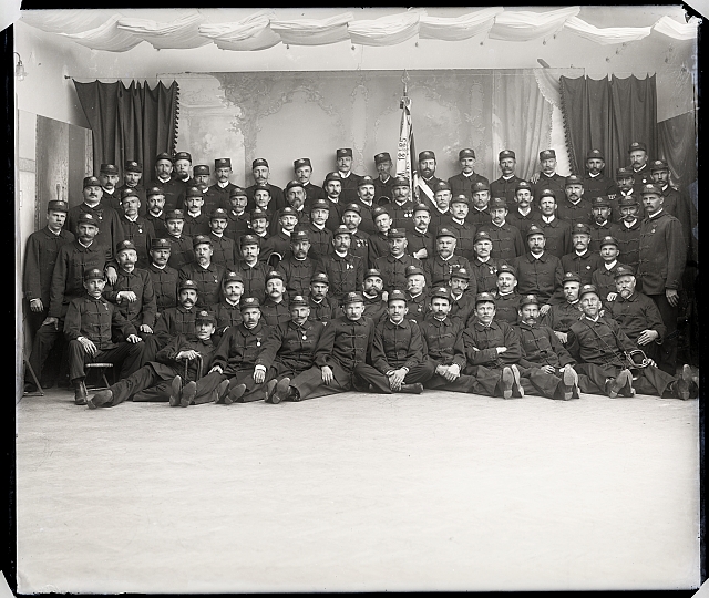 Ateliérový snímek - hasičská skupina, 1885 4.6.  Na krabičce: 613, 205 v kroužku 11ks-sklo  - Odbočka U.J.Č.Č (číšníci) - plesový... skupina